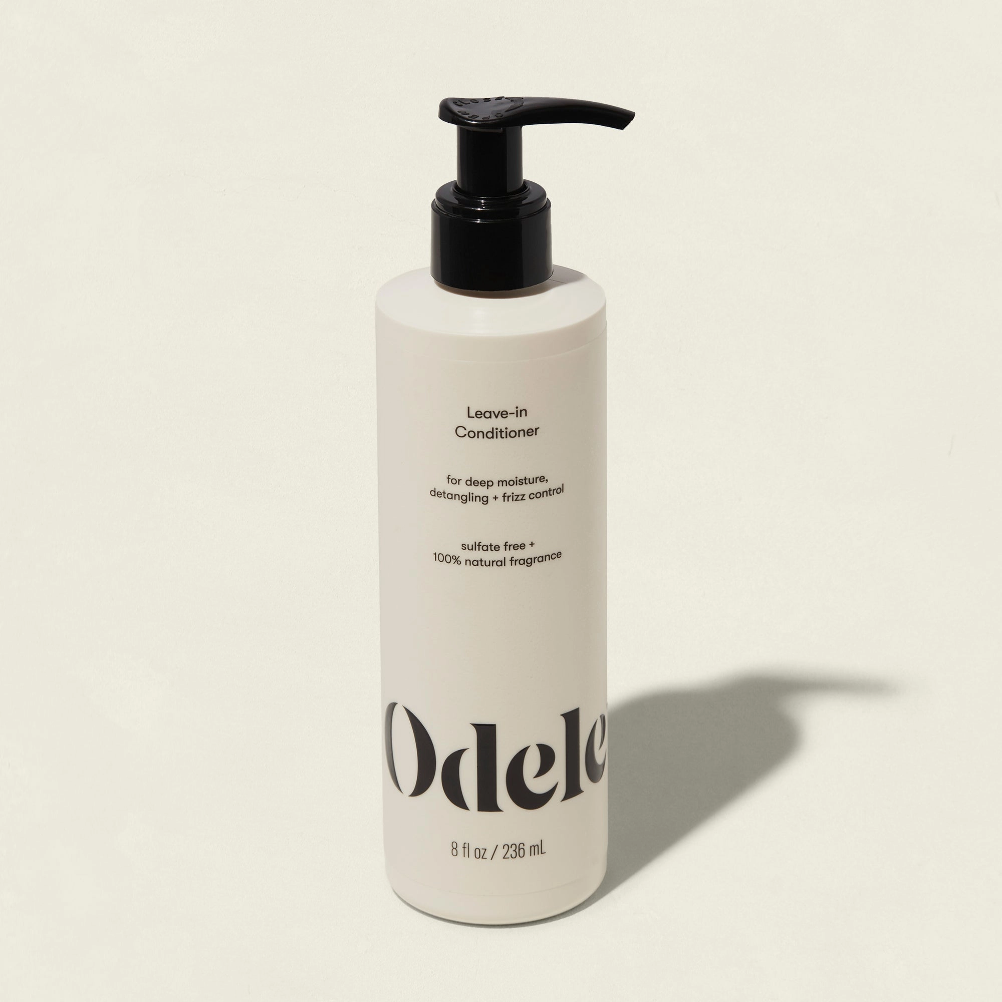 A white bottle of Odele Leave-in Conditioner with a black pump on a plain light background