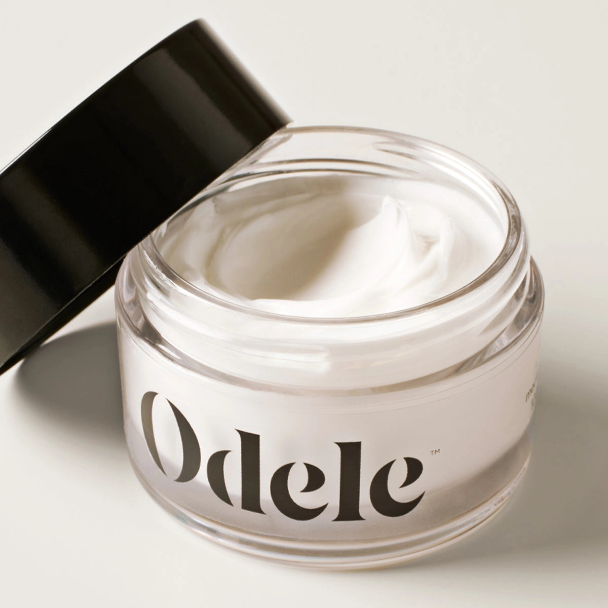 An open jar of Odele Cream Pomade with a black lid leaning against the side
