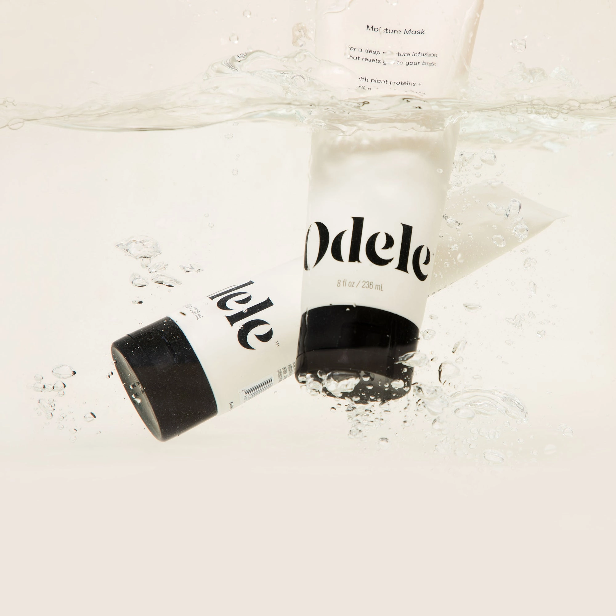 Two Odele Beauty Moisture Mask tubes are partially submerged in clear, bubbly water