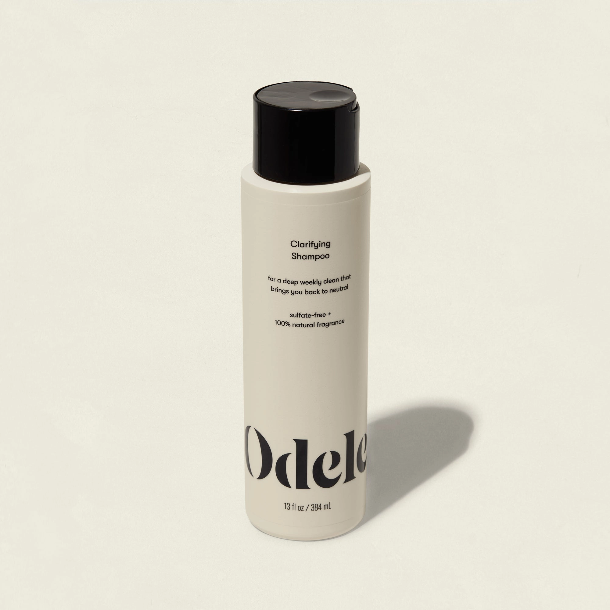 A bottle of Odele Clarifying Shampoo with a black cap on a light beige background