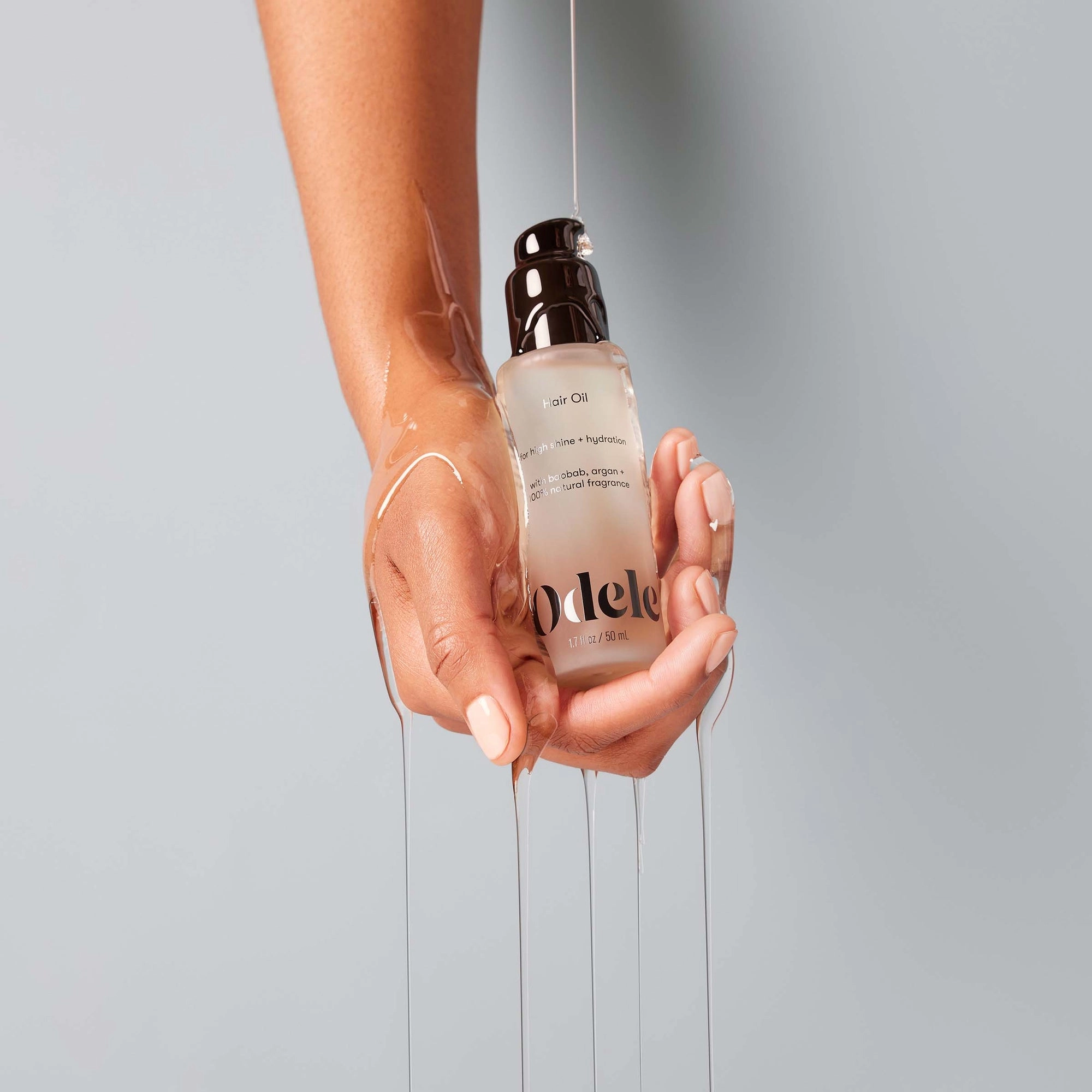 A hand holds Odele Hair Oil Mini, with the lightweight oil streaming down the wrist and fingers