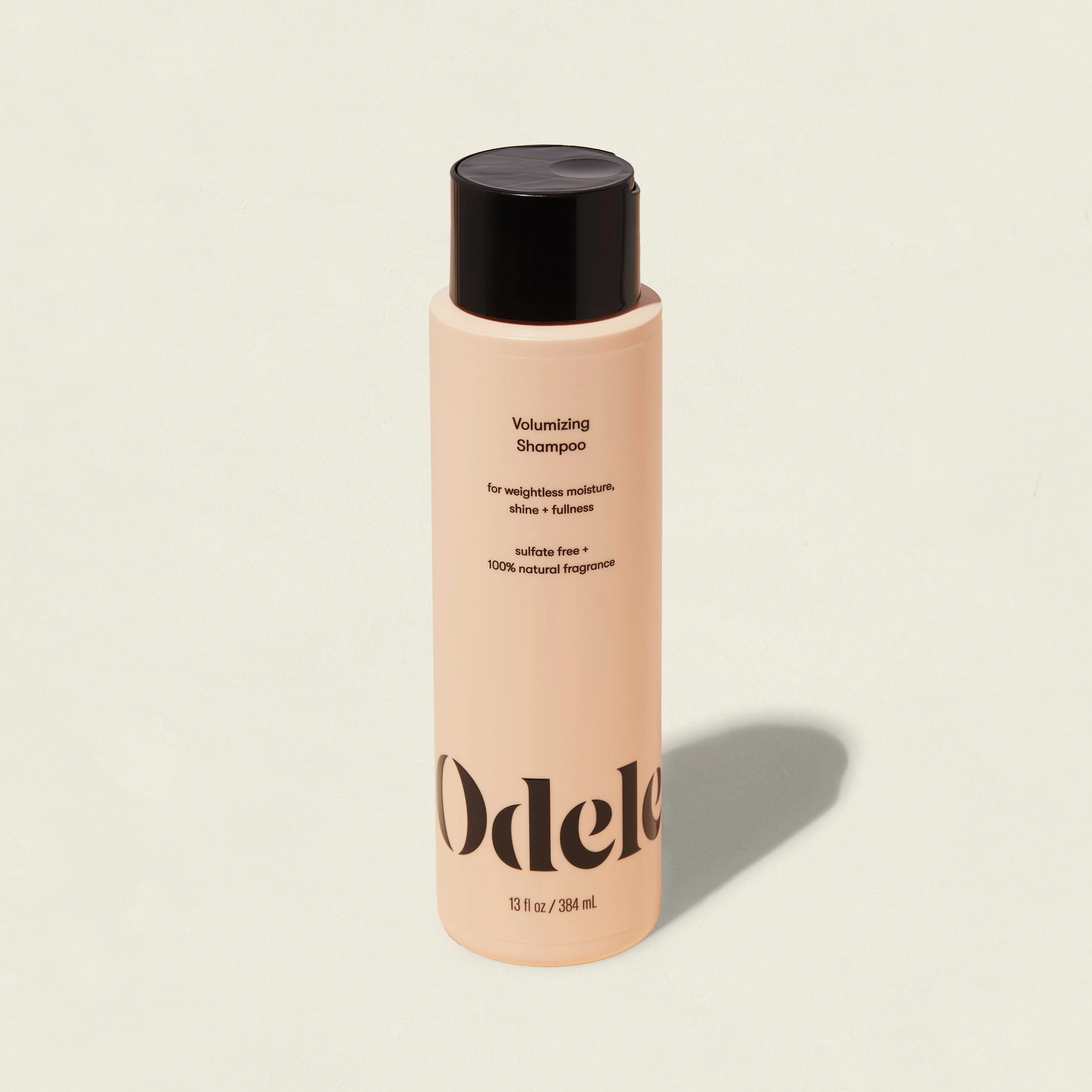 A peach-colored bottle of Odele Volumizing Shampoo with a black cap and minimalist black text