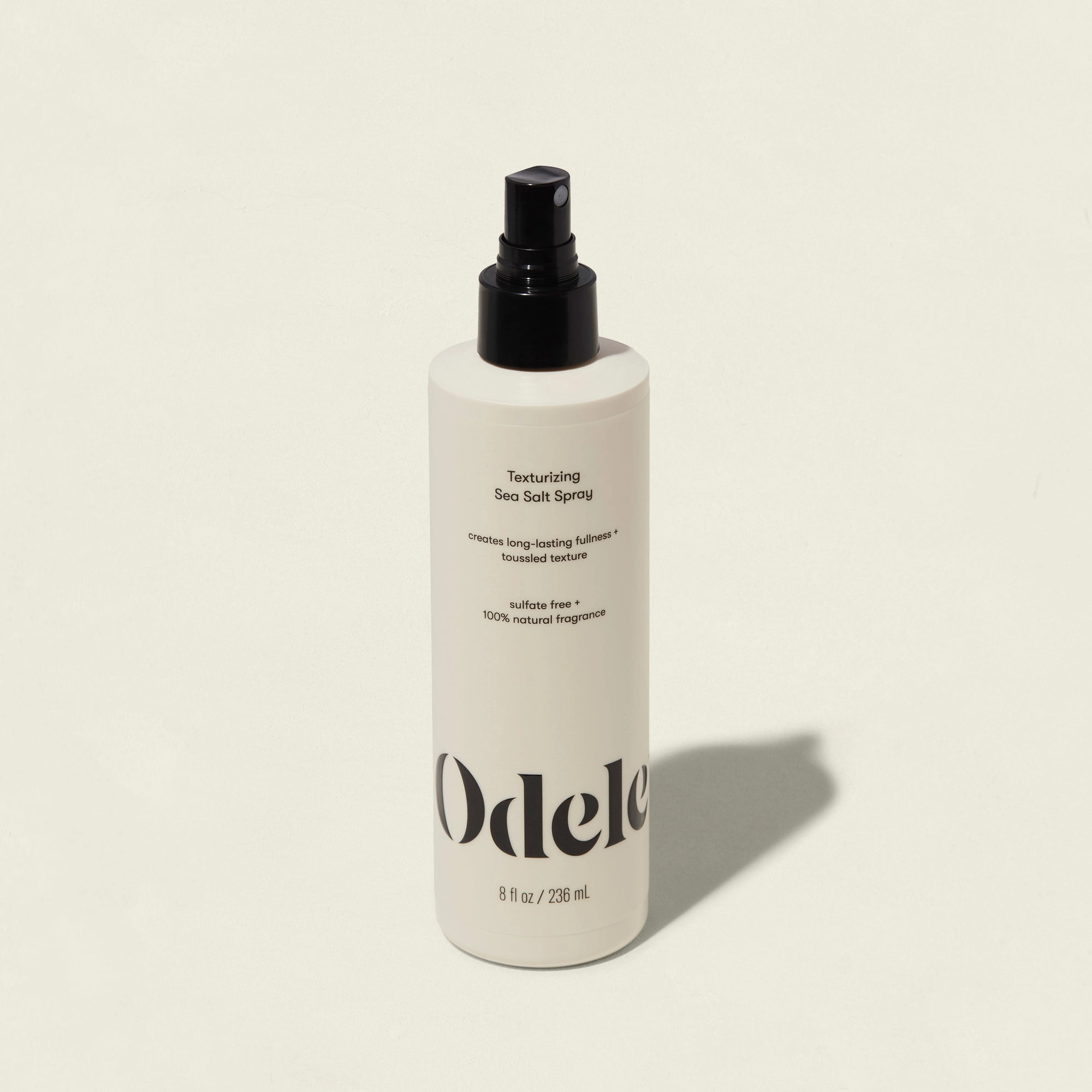 A white bottle of Odele Texturizing Sea Salt Spray with a black nozzle on a light background