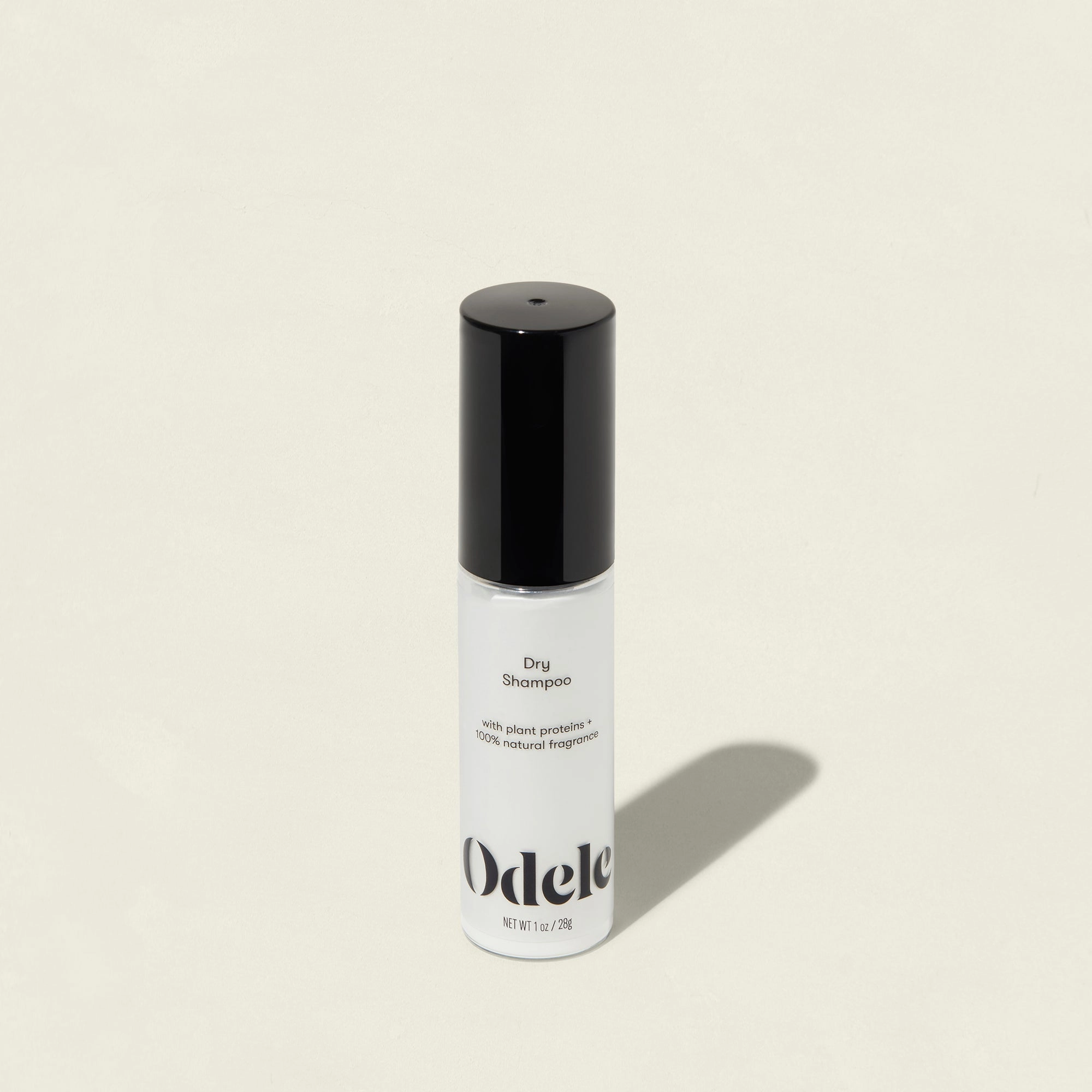 A white bottle of Odele Dry Shampoo with a black cap on a light beige background